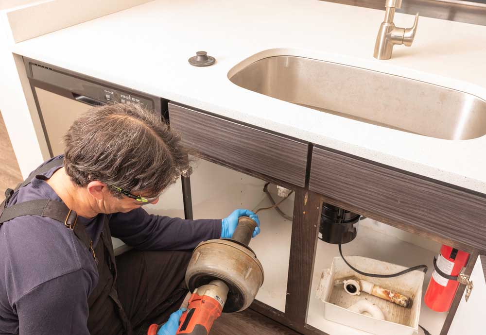 Plumber using an electric snake to unclog a kitchen sink Plumber using an electric snake to unclog a kitchen sink